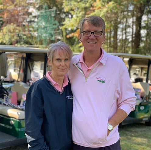 A smiling man and woman in golf attire pose for a photo near golf carts.