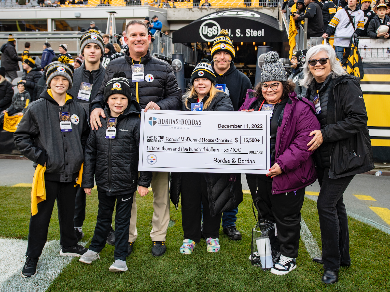 A group of people in Pittsburgh Steelers apparel pose with a large check for Ronald McDonald House Charities.